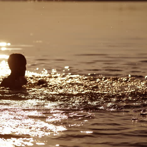 silhouette of boy splashing water in the river. evening background and two boys playing in the water happily. healthy childhood.