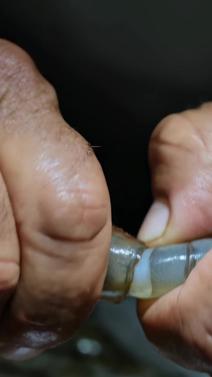Video verticale: Mani che afferrano la coda di un gambero, sbucciano il guscio e rimuovono il filo intestinale per cucinare sul bancone della cucina