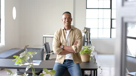smiling businessman sitting on desk in modern office with plants around