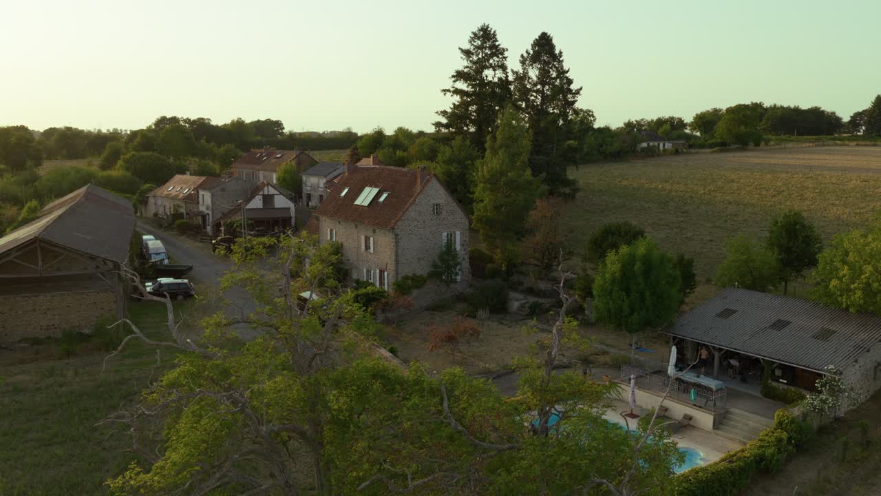Aerial view of a countryside village with stone houses, barns, and winding roads glowing in warm sunset light