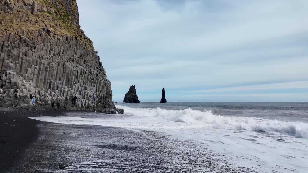 una vista impresionante se desarrolla, donde majestuosas montañas se encuentran con la playa serena, bajo un lienzo de nubes y cielo azul, playa de arena negra