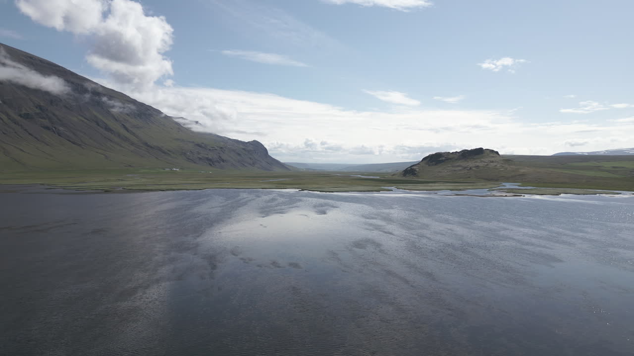 Wind blows over lake at edge of flood plain in valley, sky reflects in water, aerial