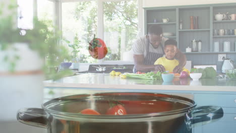 animation of tomatoes falling over happy african american father and son cooking together