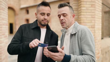 una pareja joven usando un teléfono inteligente y una tarjeta de crédito en la calle.