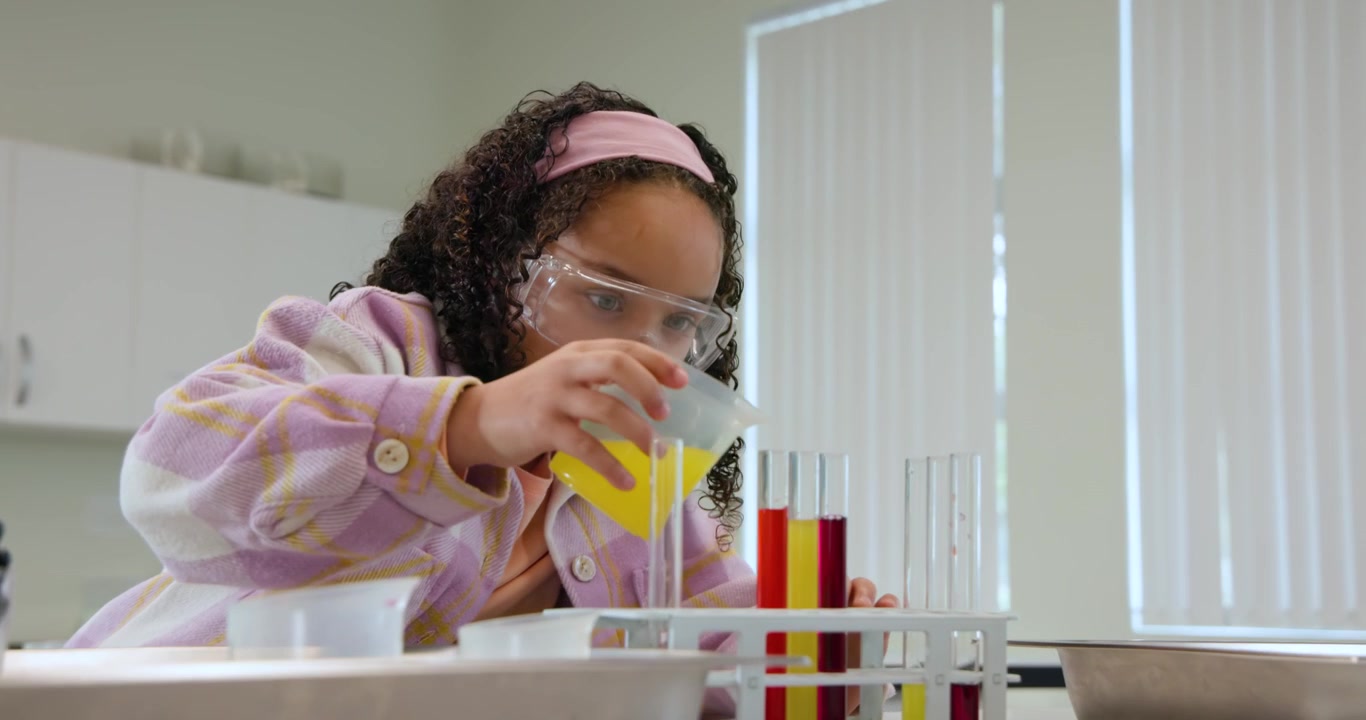 African American teen wearing goggles picking beaker pouring liquids into tubes for lab class