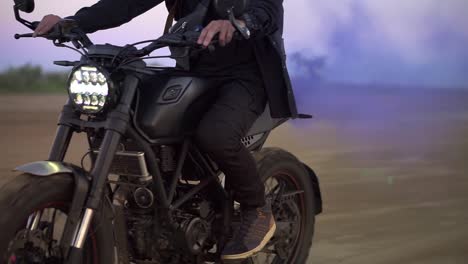 Unrecognizable-biker-in-black-riding-while-the-engine-blowing-out-blue-exhaust-smoke,-holi