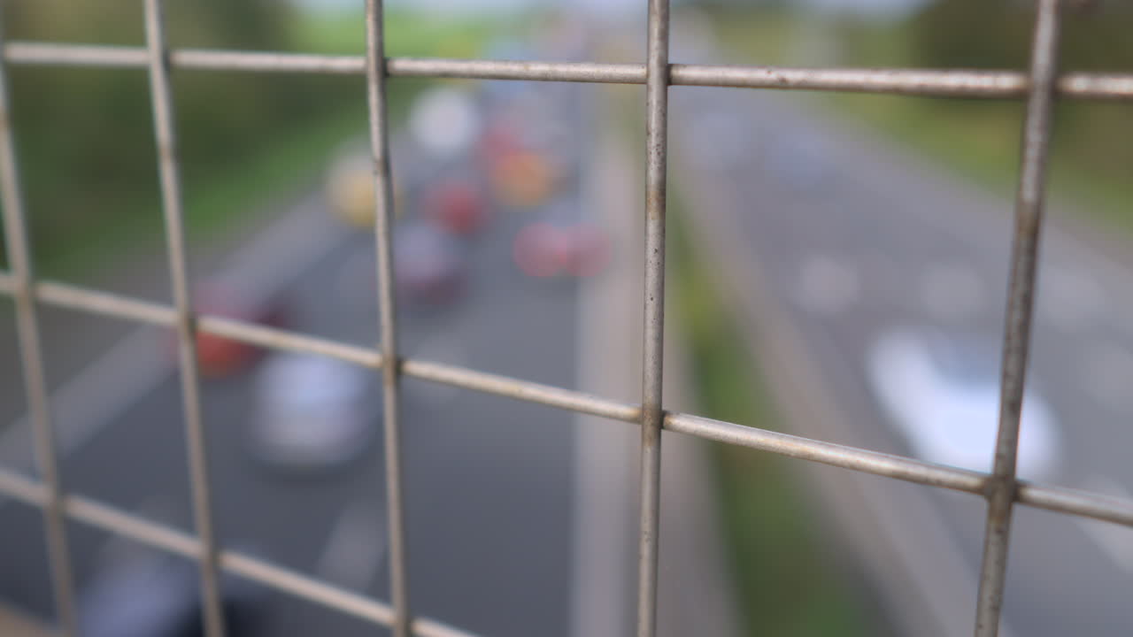 Traffico in movimento sfocato su un'autostrada britannica con vista attraverso una recinzione a maglie a fuoco.