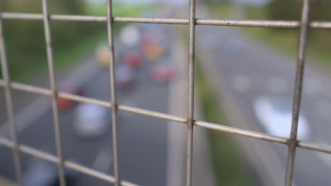 Tráfico-En-Movimiento-Borroso-En-La-Autopista-Británica-Con-Vistas-A-Través-De-Una-Valla-De-Malla-Enfocada