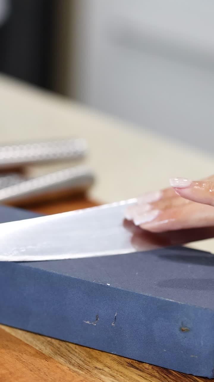 A person sharpens a knife on a whetstone in a well-lit kitchen environment