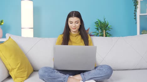 una joven estudiante linda y feliz mirando la computadora portátil en casa, estudiando, enviando correos, escribiendo textos.