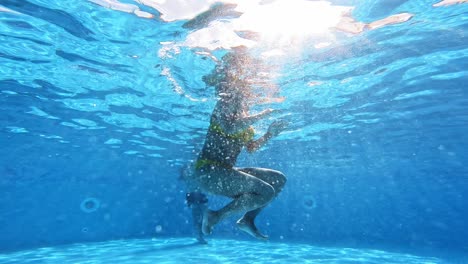 Underwater view of a young woman in a swimming pool. Woman in yellow swimsuit is swimming in the pool in summer.