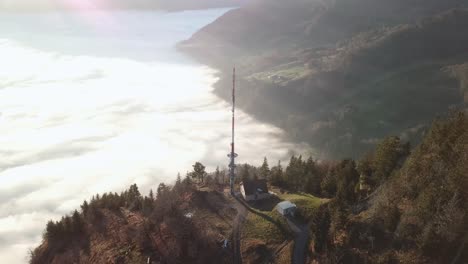 estación base de red con un gran mástil de transmisor de radio en el borde de una ladera de montaña por encima de la cubierta de nubes bajo el sol brillante