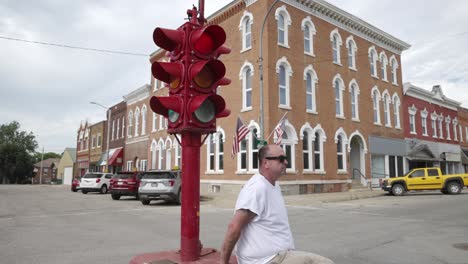 hombre con camisa blanca y gafas de sol sentado en la base de un antiguo semáforo de cuatro vías en el centro de toledo, iowa con video moviéndose por detrás