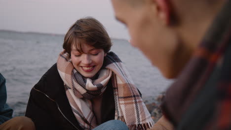 camera focuses on a teenage girl roasting marshmallows over the fire while talking to a friend who is sitting in front of her