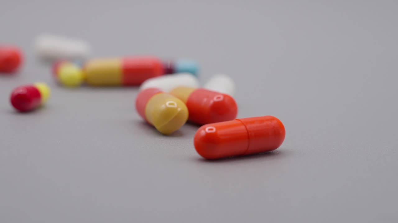 PLANO A CÁMARA LENTA DE UNAS PASTILLAS RODANDO POR UNA SUPERFICIE GRIS