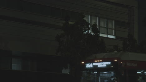 Close-up-Shot-Of-Light-Escaping-Through-The-Blinds-In-The-Police-Station-At-Night-With-Traffic-Passing-Past