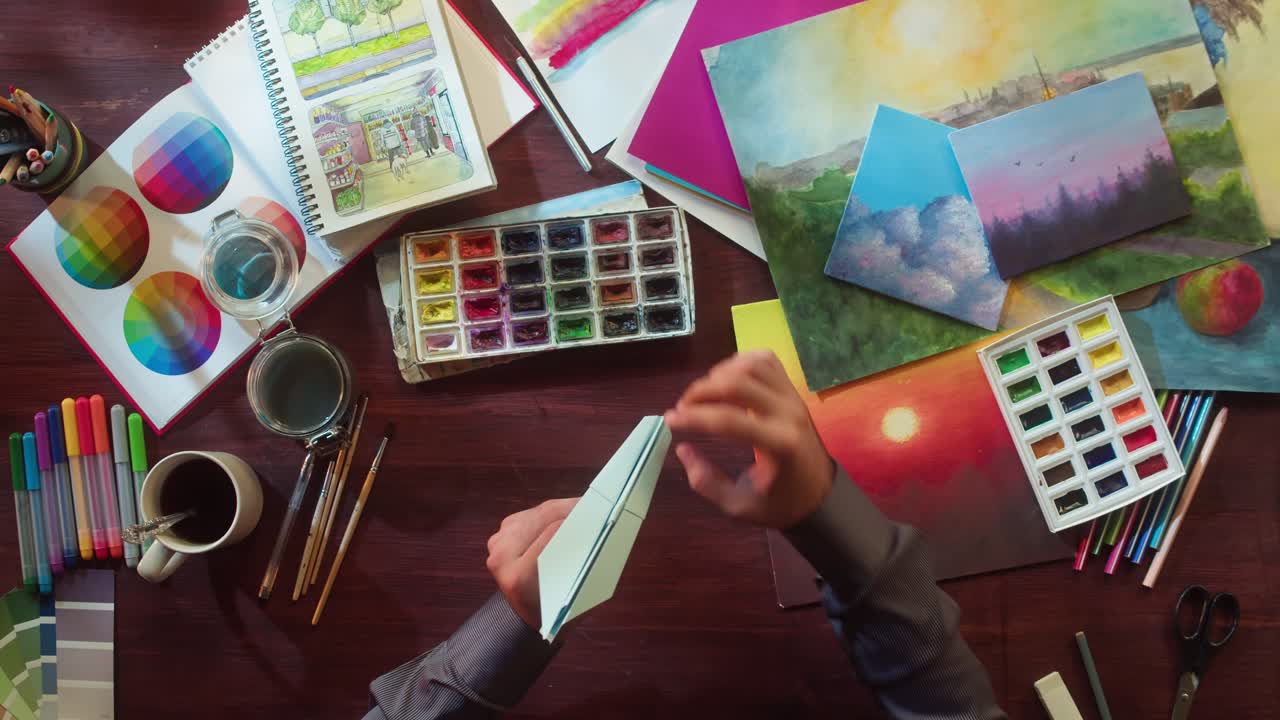 Top View of Hands Making a Paper Airplane on an Artist's Desk