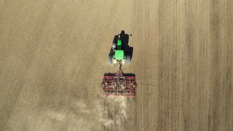 Low-altitude-aerial-top-down-view-of-green-double-wheeled-tractor-cultivating-agricultural-field