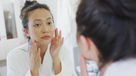 happy asian woman looking at mirror and touching face in bathroom, in slow motion