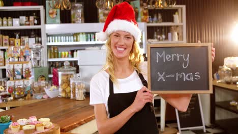 Portrait-of-waitress-showing-chalkboard-with-merry-x-mas-sign