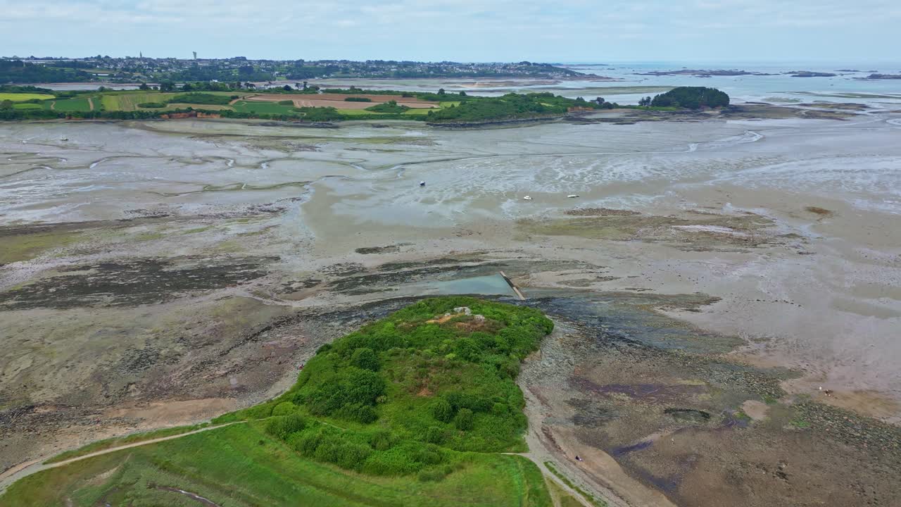 Drone flies forward over sandy Paimpol Bay at low tide, revealing the coastline and distant view of the town - France