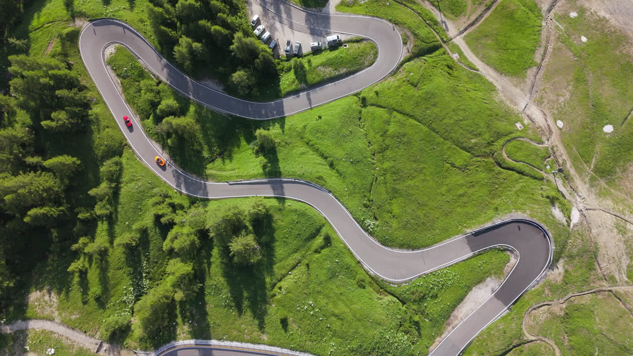 Drone captures two supercars driving on a curvy mountain road with forest and meadows around. Scenic and dynamic. Category: Transportation