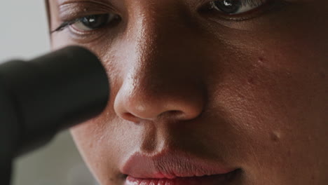 close up of female researcher looking through microscope in lab