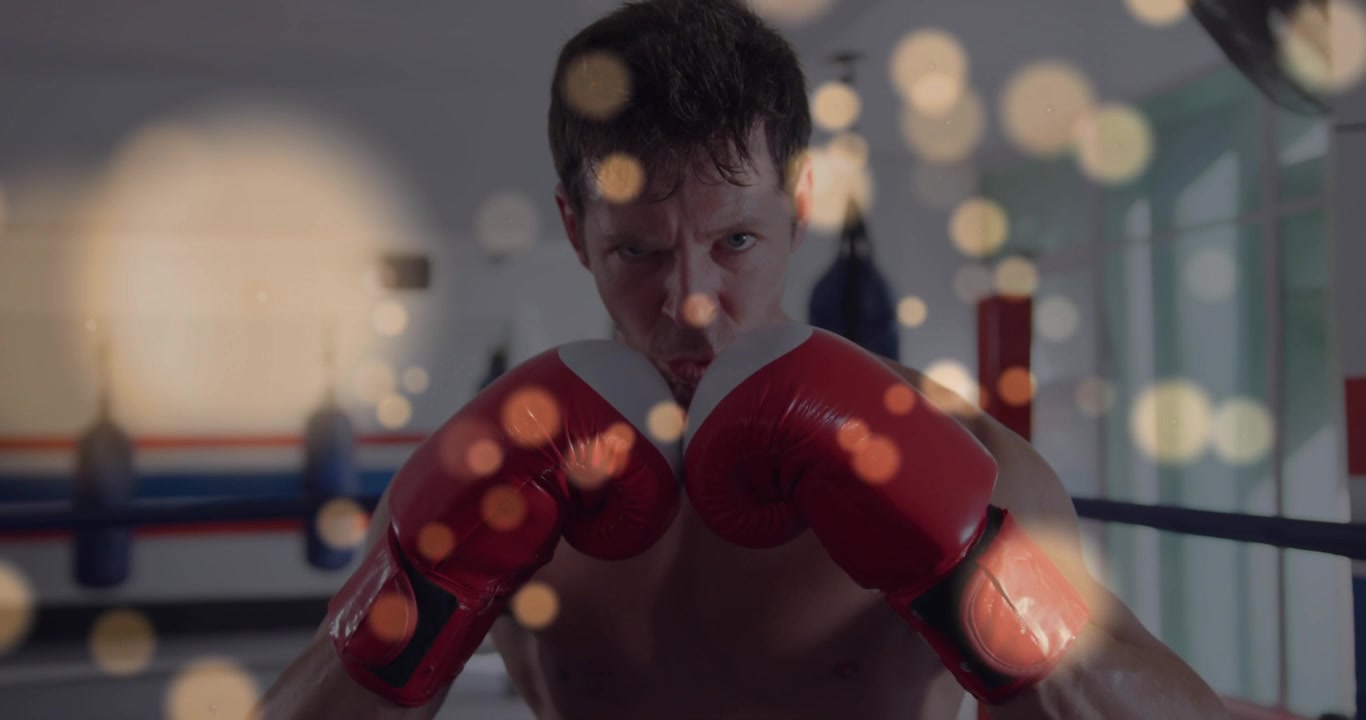 Pugile che stringe la mascella e alza i guantoni rossi, che pratica jab sul ring di pugilato con una calda sovrapposizione bokeh.