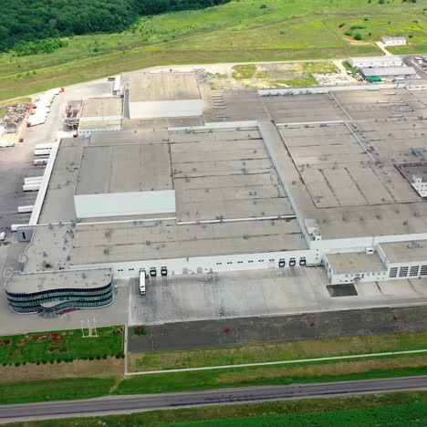 roofs of a huge industrial factory in green nature. flight over contemporary complex with parking zones on field. aerial view