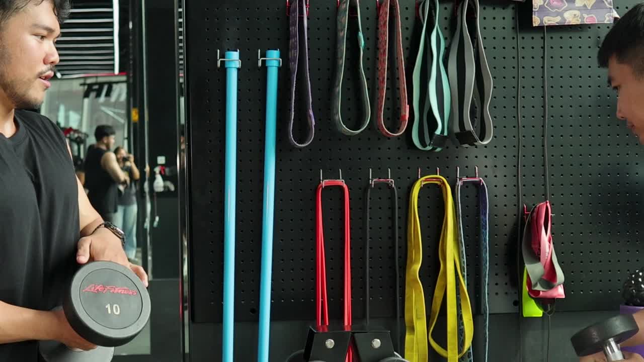 Two athletic men choose weights from a rack in front of a fitness equipment wall