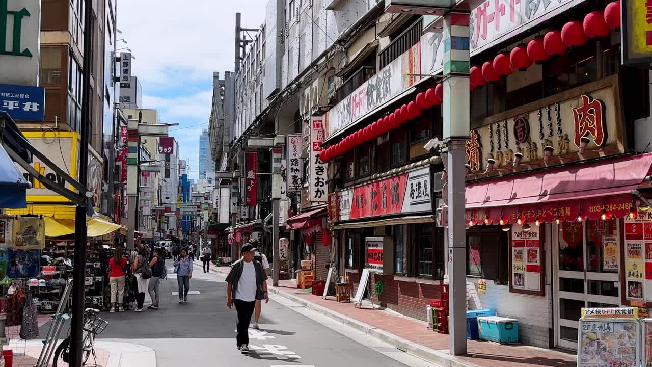 Bustling street in Ueno, Tokyo with pedestrians walking past traditional shops and restaurants