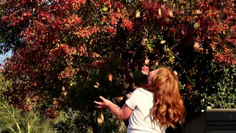 girl playing with autumn leaves under a red-leafed tree