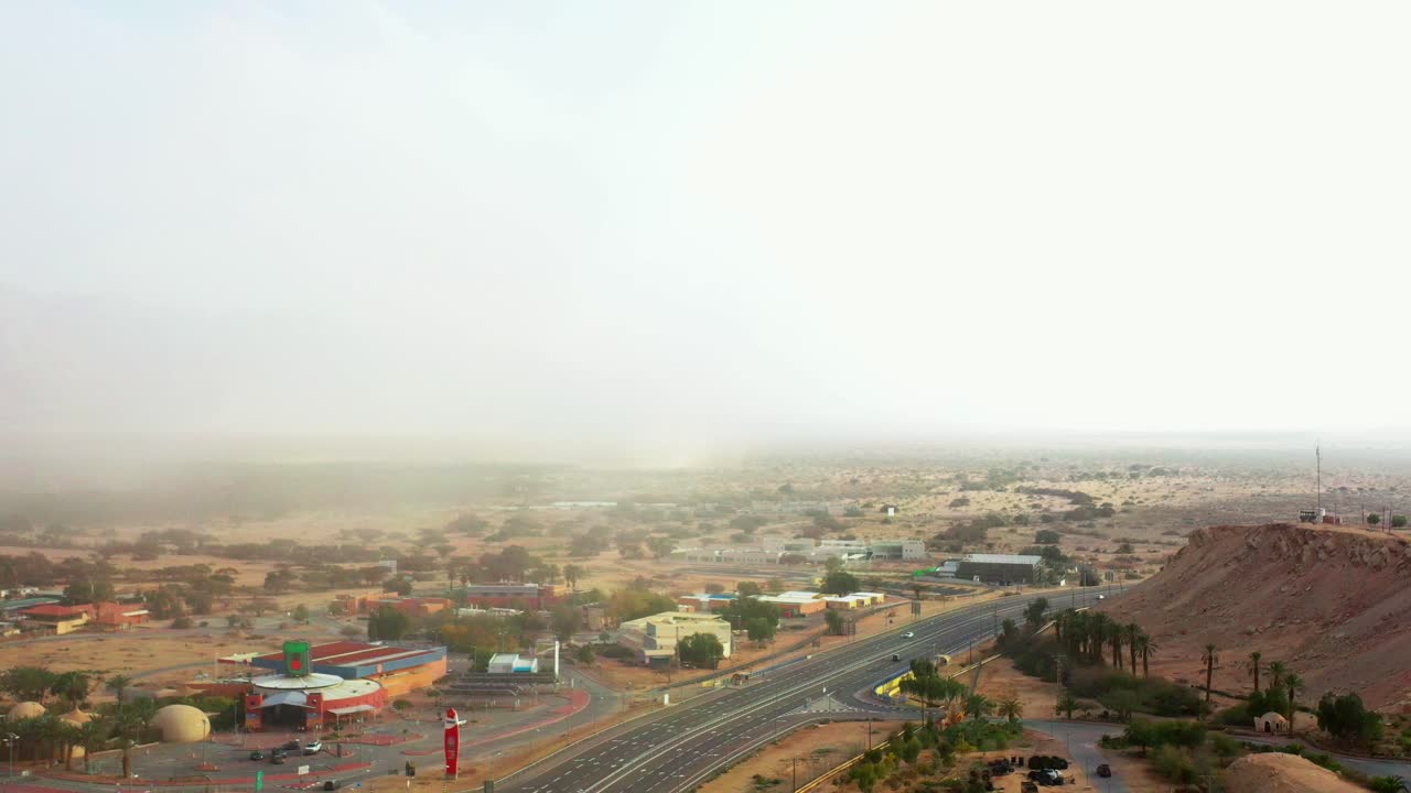 varios coches circulan por la autopista arabah road en el sur del desierto de neguev, pasando por la gran parada de la comunidad cooperativa kibutz yotvata con una gran tormenta de arena que arrasa