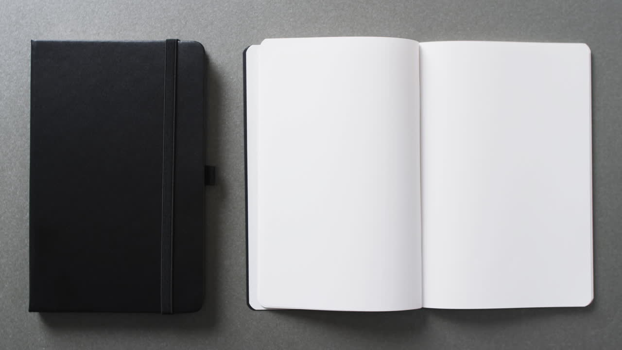 Close up of open blank book and black notebook with copy space on gray background in slow motion