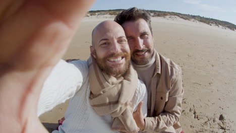 pov of a happy gay couple taking selfie on phone on the beach