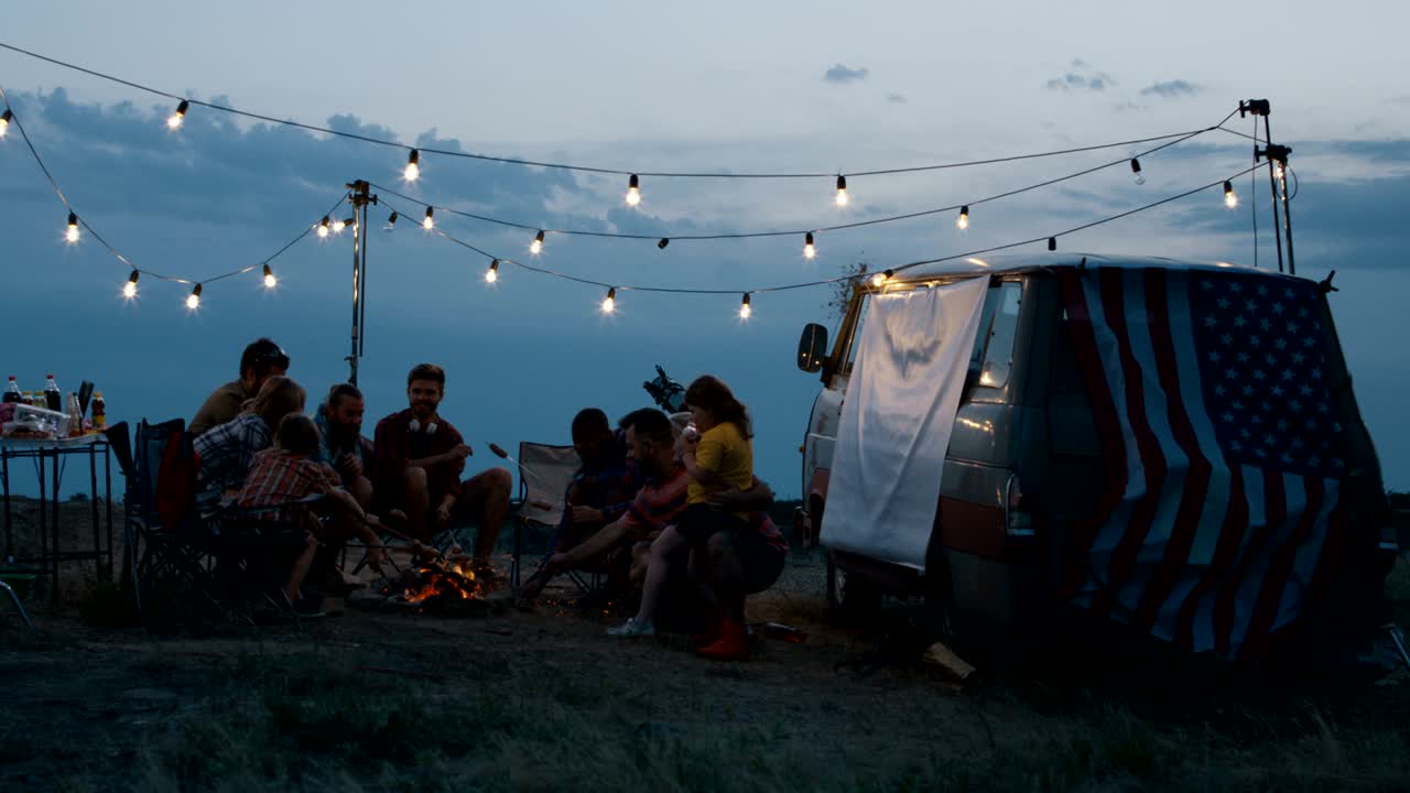 группа путешествующих друзей жарит колбасы в кемпинге.