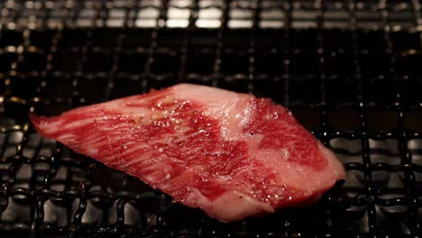 a detailed view of a marbled beef slice being placed and grilled on a wire mesh using tongs.