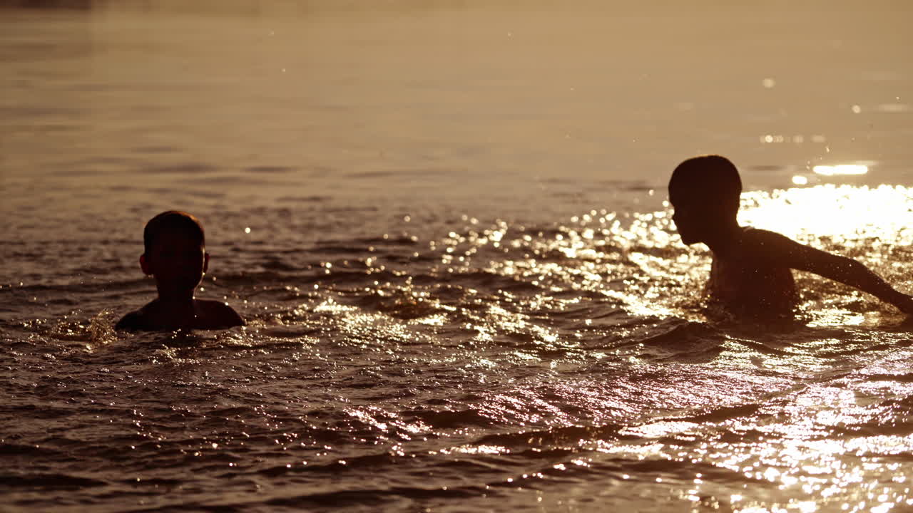 Kids playing in the evening water background. Two friends having fun together in the river while splashing with water outdoors.