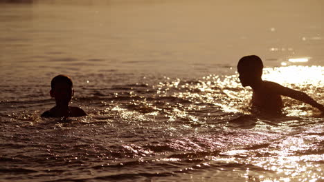 kids playing in the evening water background. two friends having fun together in the river while splashing with water outdoors.