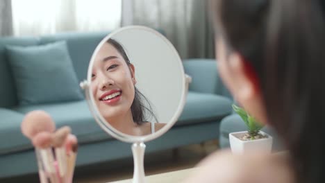 거울에 반사 된 아름다운 젊은 아시아 여성은 집에서 메이크업을 할 때 세럼을 적용하고 미소 짓고 있습니다.