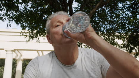 a sporty elderly caucasian man drinks water after fitness classes