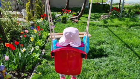 vista trasera de una niña linda con un sombrero rosa en un columpio en el patio trasero