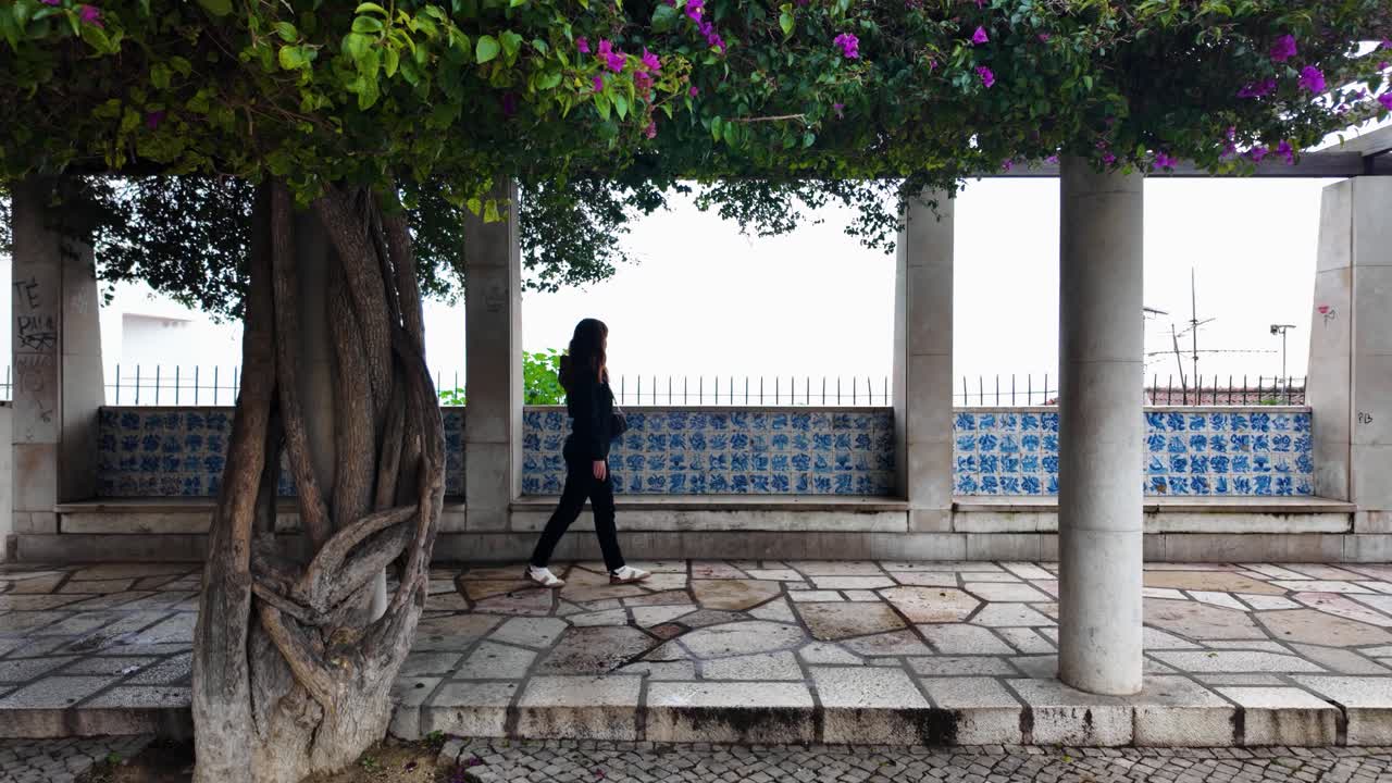 Slowmotion of girl walking at Miradouro de Santa Luzia with mosaic wall