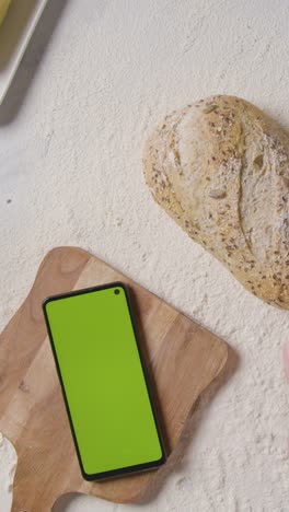 Vertical-Video-Overhead-Shot-Of-Person-Putting-Loaf-Of-Bread-Onto-Floured-Kitchen-Surface-With-Green-Screen-Mobile-Phone