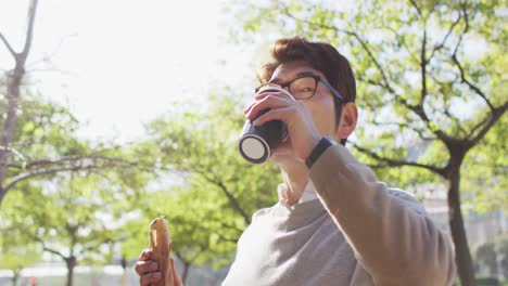 asian man drinking coffee and having a snack while walking outdoors