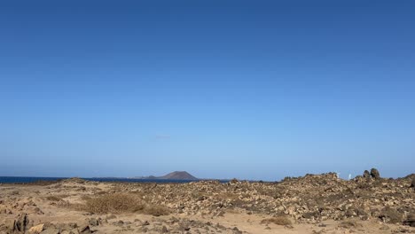 driving pov shot of the arid, volcanic landscape in northern fuerteventura, with the ocean and isla de lobos visible in the distance. canary islands, spain