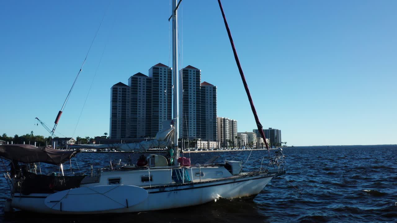 Una barca a vela scivola su acque aperte con uno sfondo di moderni grattacieli sotto un cielo azzurro limpido. Ideale per temi marittimi o di stile di vita urbano