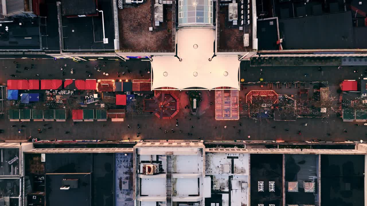 Static aerial drone shot of Southampton’s Christmas Market at sunset, showing rows of glowing festive stalls, steady crowds weaving through the square, and warm evening light with winter atmosphere