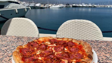 pizza tradizionale italiana di pepperoni con vista su yacht di lusso a puerto banus porto durante l'estate a marbella spagna, cibo gustoso, giorno di sole, 4k shot