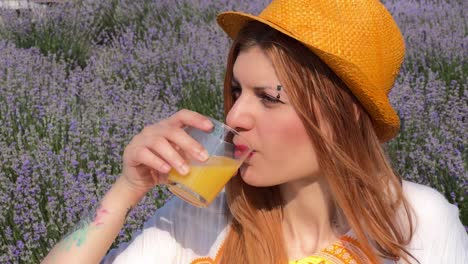 retrato de perfil lateral de una mujer joven con perforación de cejas y sombrero naranja contra un campo de lavanda